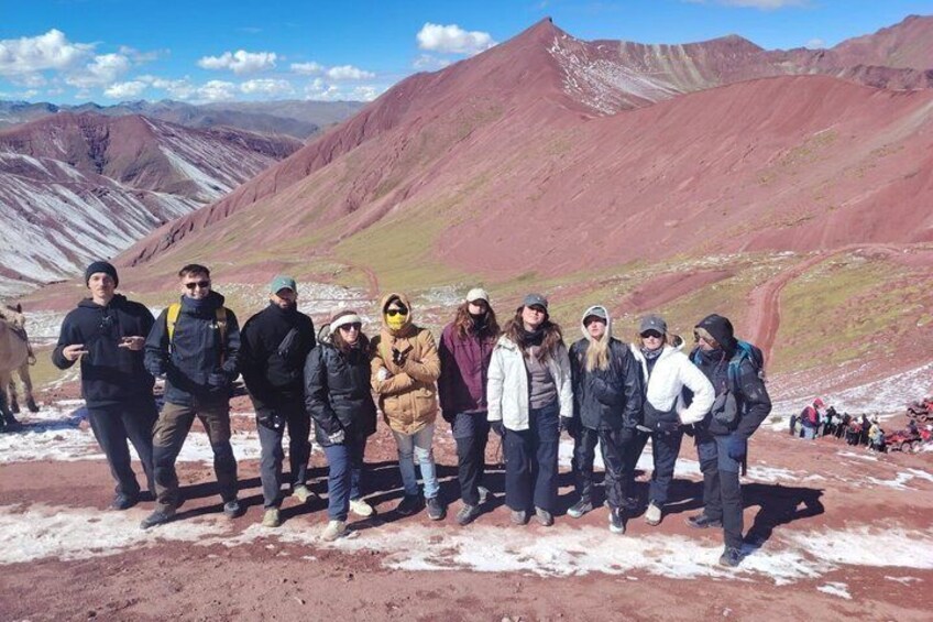 A group of people standing on a snow-covered ground with red mountains in the background. 5