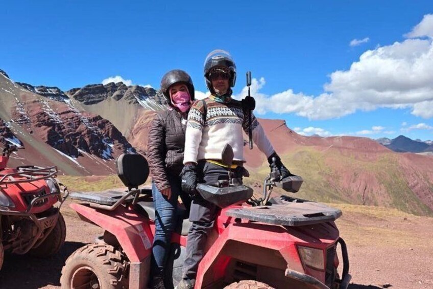 Two people on a red ATV with a mountainous landscape in the background. 2