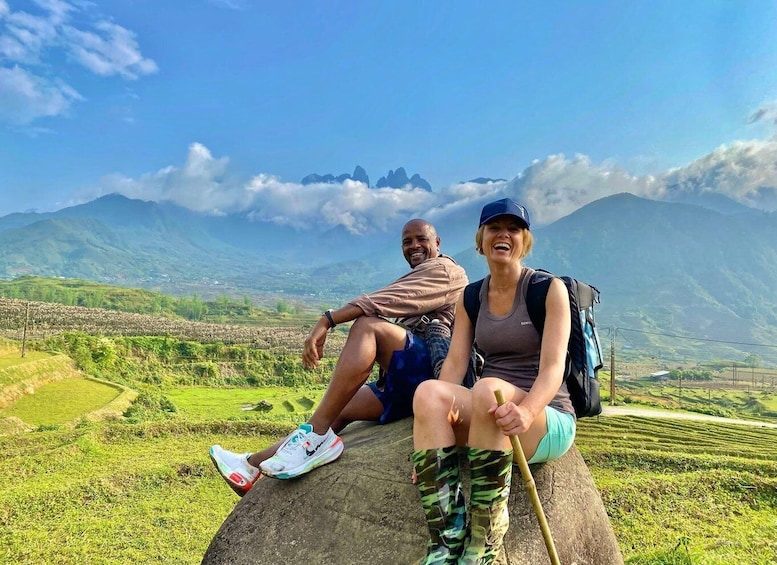 Two people sitting on a rock with a mountainous landscape in the background. 1