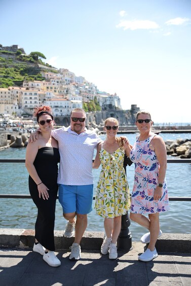 A group of people standing by a waterfront with buildings and a hill in the background. 5