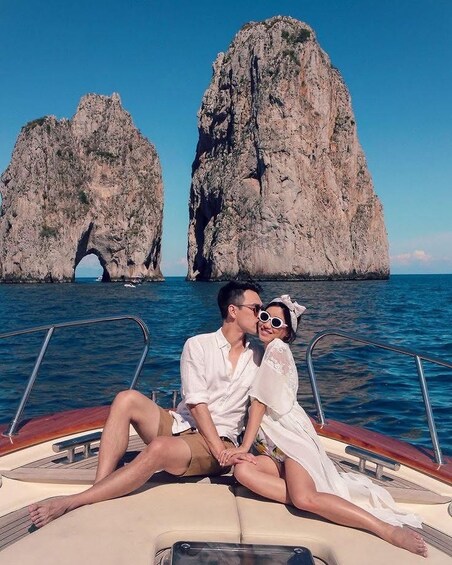A couple on a boat with a rocky coastline and two large rock formations in the background. 3