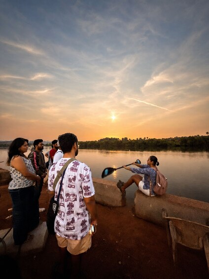 A group of people by a calm lake at sunset, with one person paddling a kayak. 4