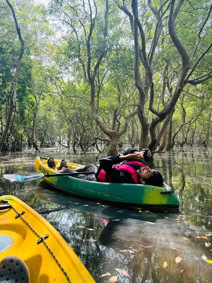 A person lying on a green kayak in a water body surrounded by trees. 5