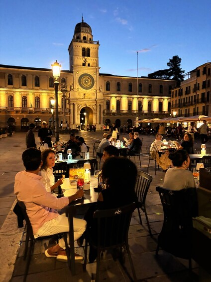 A historic square with a prominent clock tower, outdoor cafes, and people dining. 4