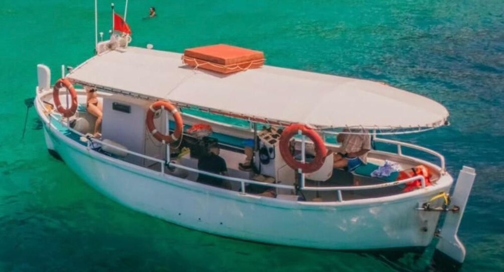 A boat with a white hull and red lifebuoys, floating on turquoise water. 1