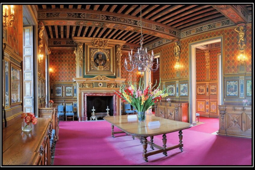 An ornate room with a chandelier, a fireplace, and a table with flowers. 2