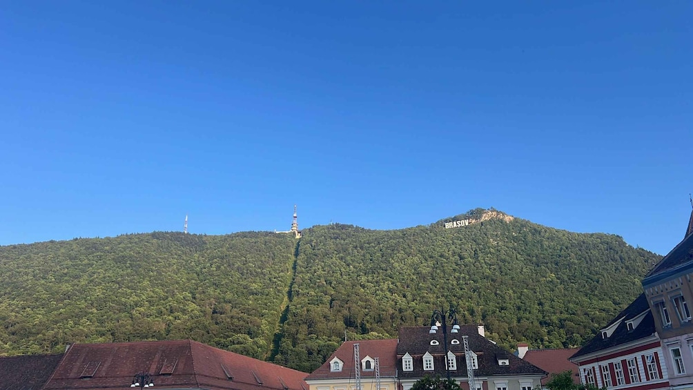 A mountain with 'BRASOV' written on it, surrounded by buildings and clear blue sky. 5