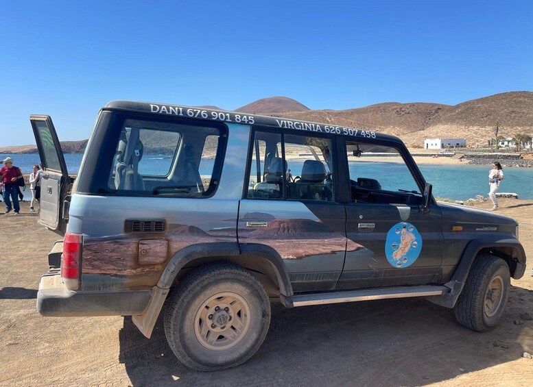 A rugged off-road vehicle parked by a beach with a clear blue sky and distant hills. 2