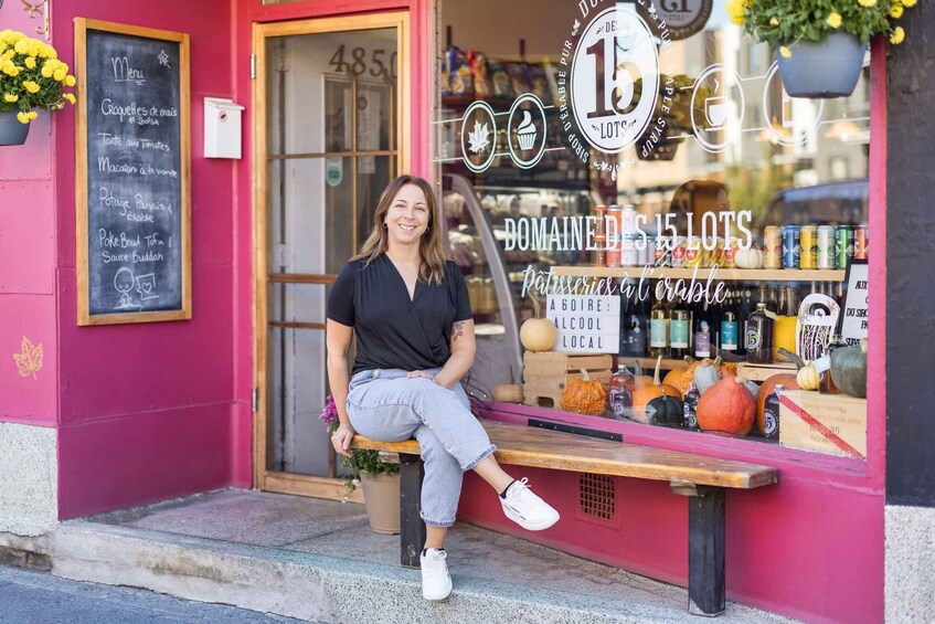 A person sitting on a bench outside a bakery with a chalkboard menu and a sign reading 'DOMAINE DES 15 LOTS.' 1