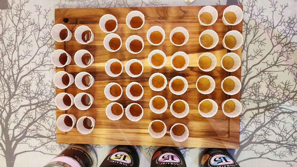 A wooden board with multiple paper cups arranged in rows, and bottles of beer at the bottom. 2