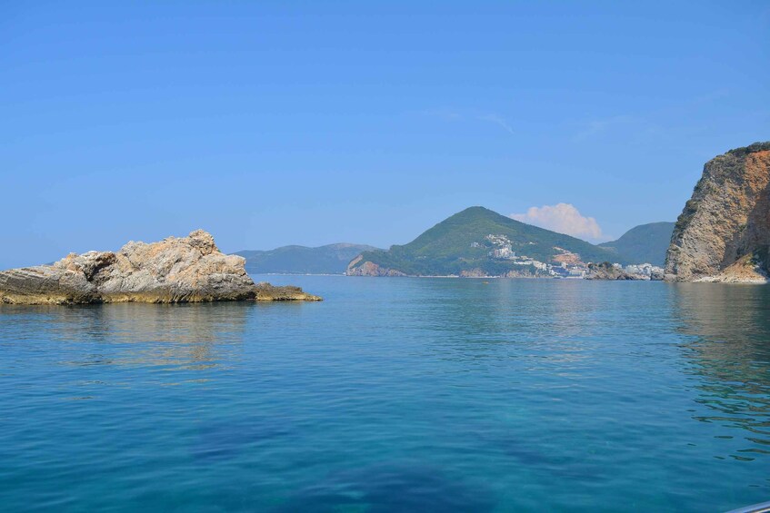A coastal landscape with clear blue water, rocky outcrops, and distant hills. 3