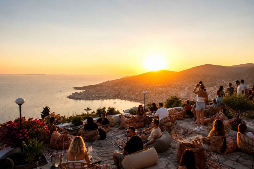 A sunset view over a coastal city with people relaxing on outdoor seating. 2