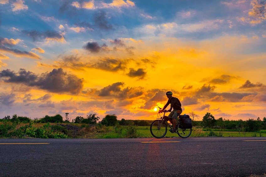 A cyclist on a road during sunset with a vibrant sky. 1
