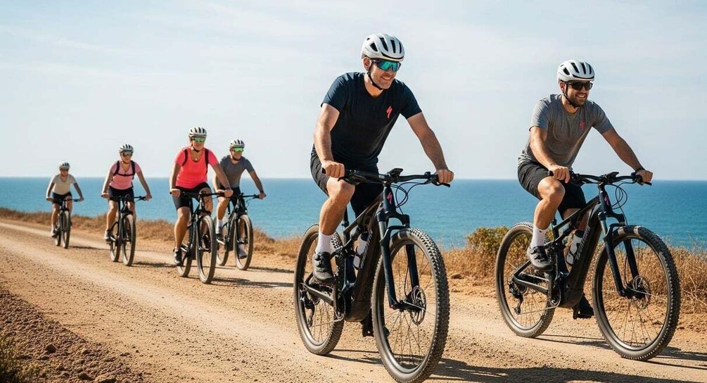 A group of cyclists on a dirt road with the ocean in the background. 4