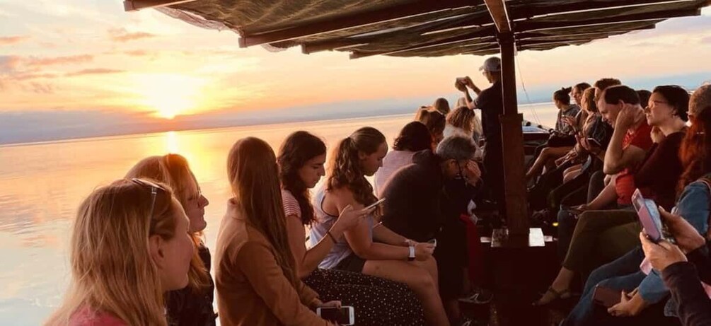 A group of people seated on a boat during sunset. 4