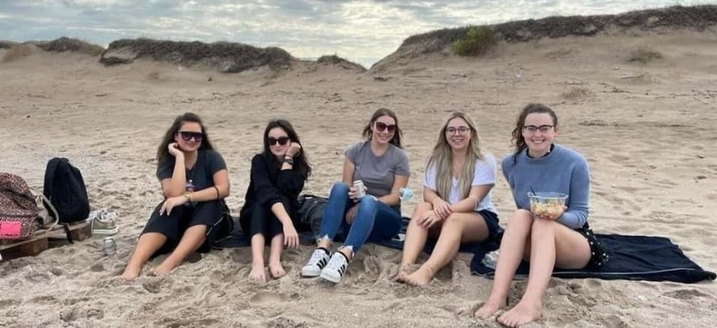 Five people sitting on a sandy beach with dunes in the background. 2