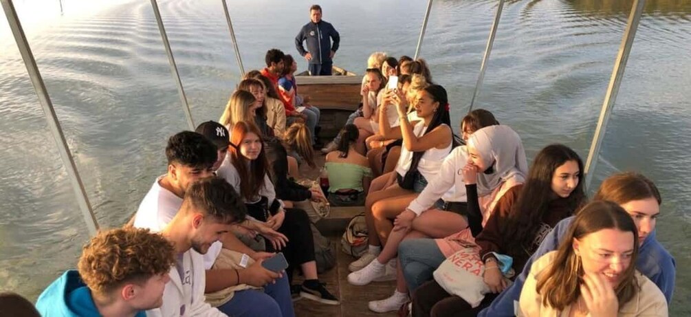 A group of people on a boat, some holding phones, with calm water and a clear sky in the background. 5