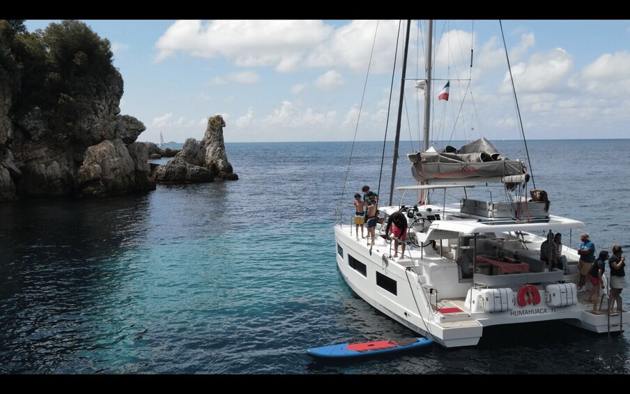 A white yacht named HUMAUACA anchored near rocky cliffs with clear blue water. 2