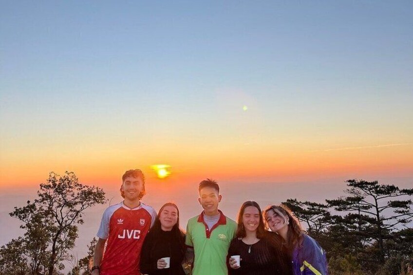 A group of people posing for a photo with a sunset in the background. 1