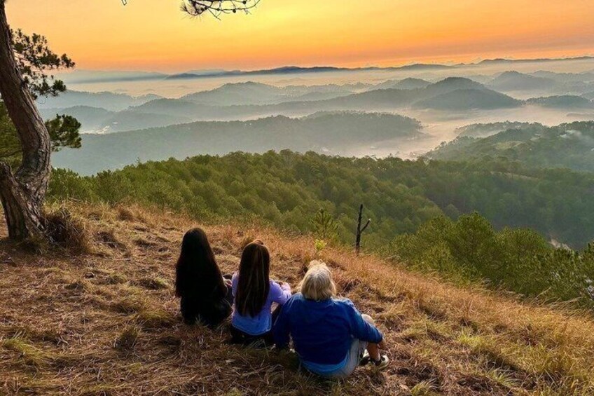Two people sitting on a grassy hill overlooking a mountainous landscape during sunset. 5