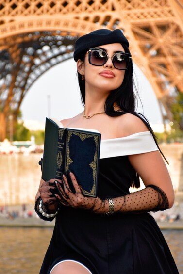 A person holding a book with a gold cover, standing in front of the Eiffel Tower. 2