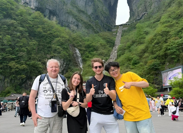 A group of people posing in front of a large rock formation with a bridge. 1