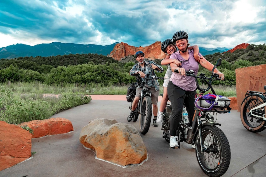 Three people on bicycles in a natural landscape with mountains in the background. 1
