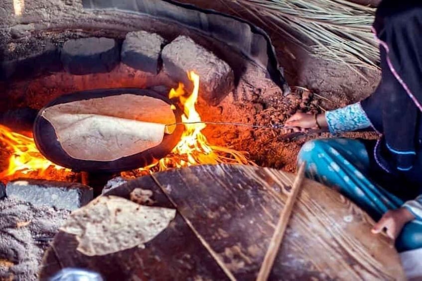 A person cooking food over an open fire in a traditional outdoor oven. 2