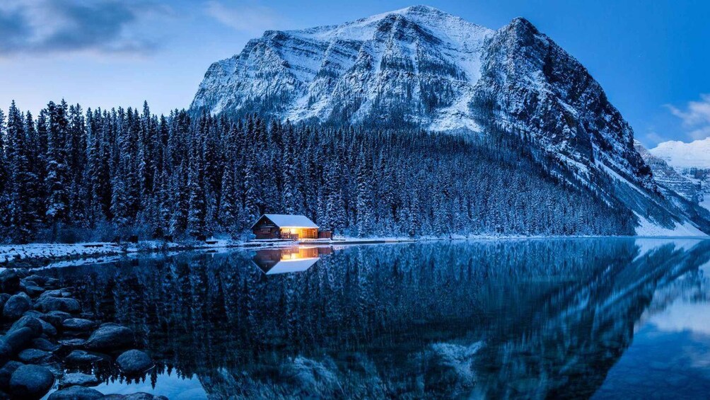 A cabin by a calm lake with snow-covered mountains in the background. 5