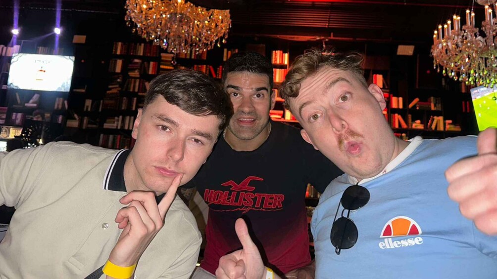 Three people in a bar with bookshelves and chandeliers. 3