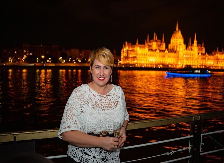 A person holding a glass, standing in front of a brightly lit building with a river in the background. 3