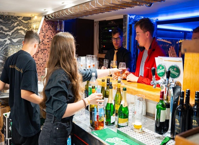 A bar with people, bottles, glasses, and a bartender. 5
