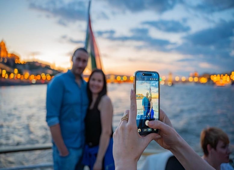 A person taking a photo of a couple on a boat with a city skyline in the background. 4