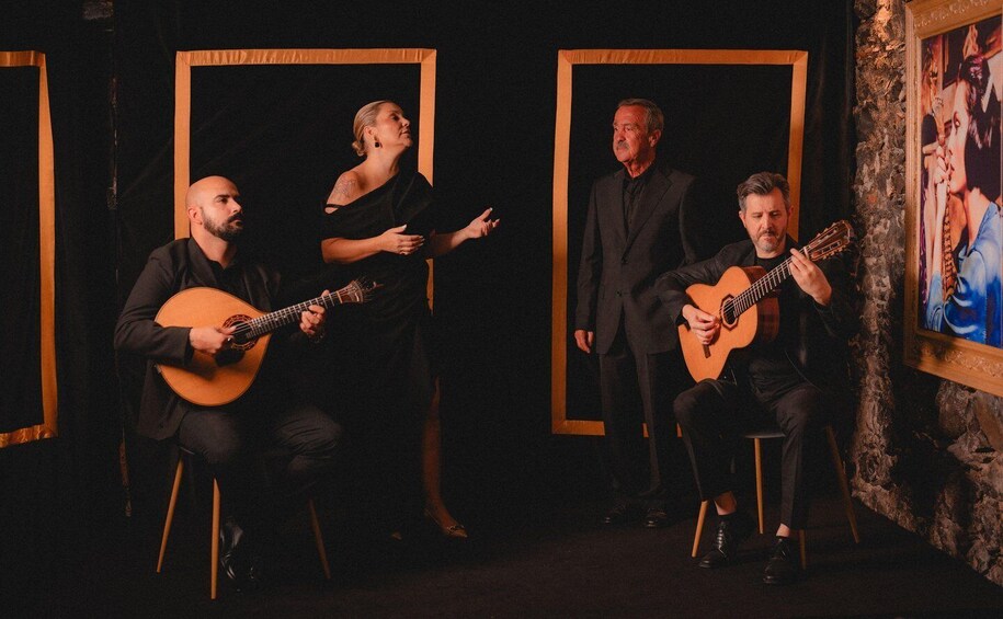 A group of people performing music with guitars in a dimly lit room with framed artwork on the walls. 1