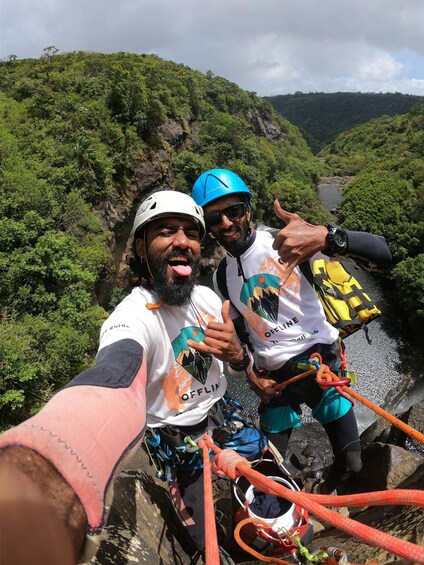Two people rappelling down a rocky cliff with a river in the background. 4