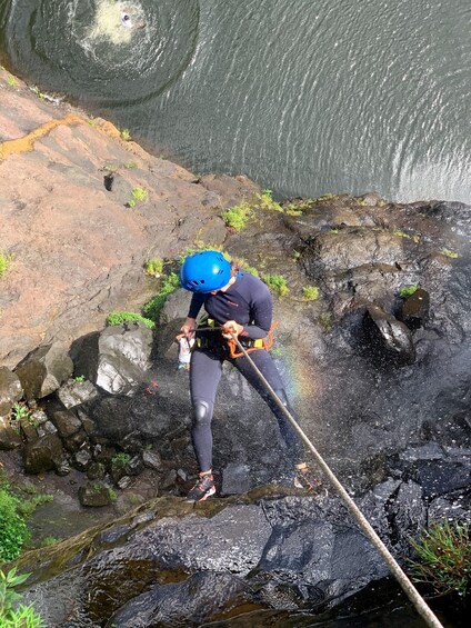 A person rappelling down a rocky cliff with a harness and helmet. 1