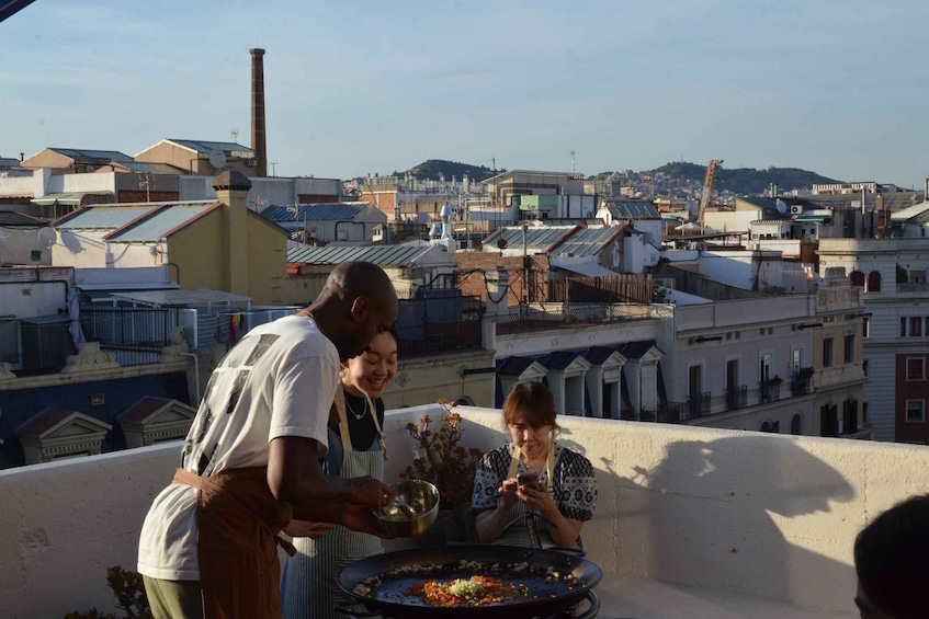A group of people cooking on a rooftop with a cityscape in the background. 1