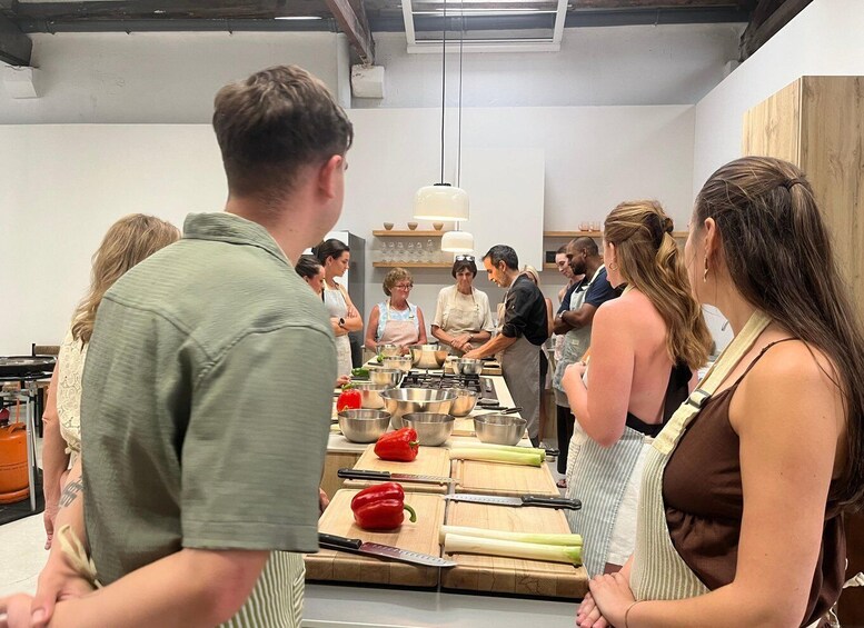 A group of people in a kitchen, some wearing aprons, with cooking utensils and vegetables on the counter. 5