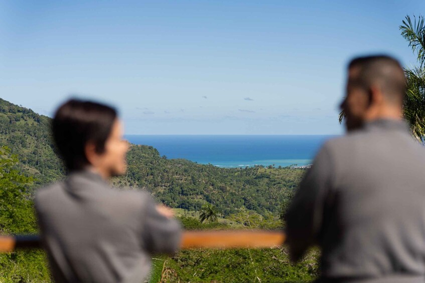Two people overlooking a coastal landscape with dense greenery and a view of the ocean. 3