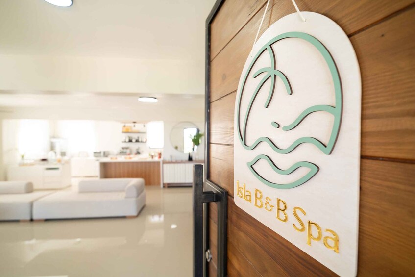A spa entrance with a logo, a wooden door, and a modern interior with a white sofa and kitchen in the background. 5