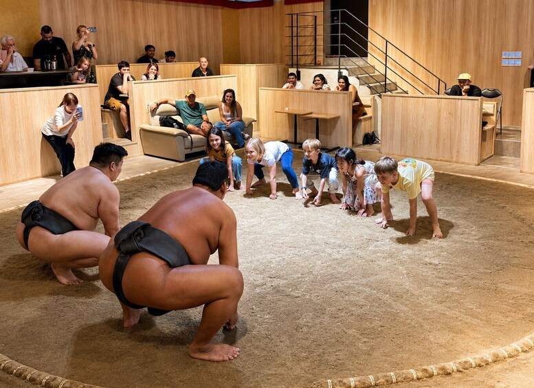 A sumo wrestling match with participants and spectators in a wooden-walled indoor arena. 5