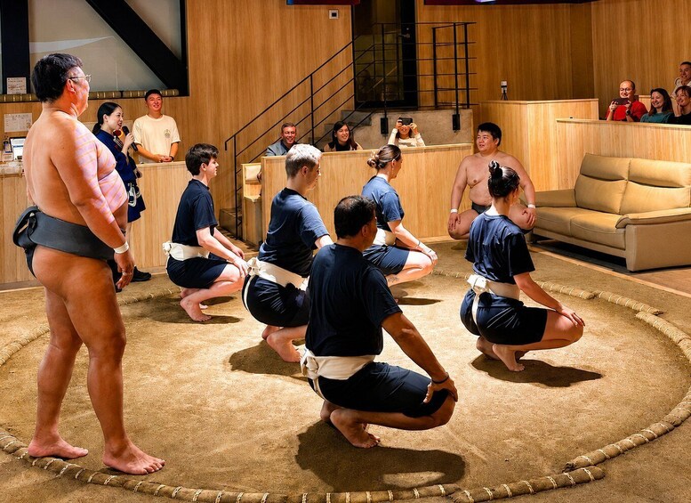 A sumo wrestling match with participants in traditional attire, a wooden floor, and spectators in the background. 1