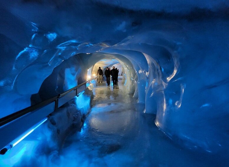 An ice tunnel with a metal railing and people walking through. 4