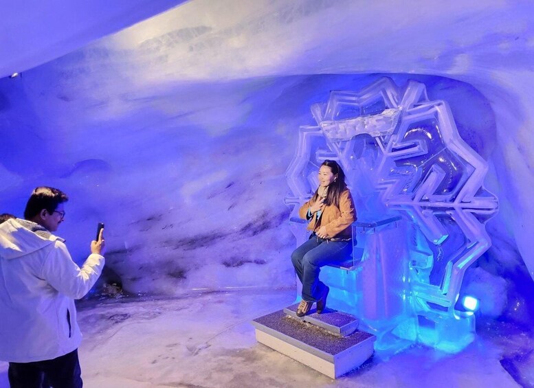 A person sitting on an ice sculpture in a blue-lit ice cave. 1