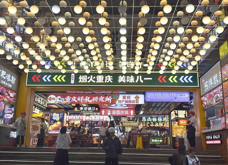 A bustling street market with numerous food stalls and overhead hanging lights. 2