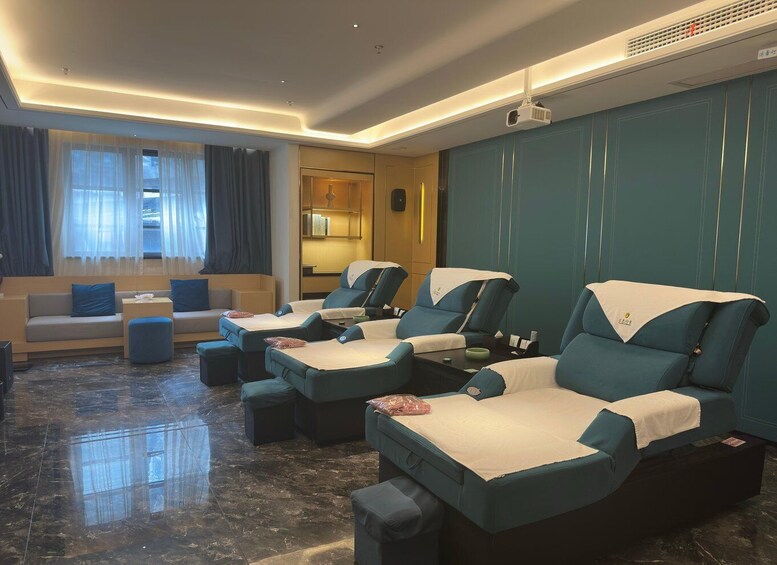 A modern relaxation room with massage chairs, a sofa, and a large window with curtains. 3