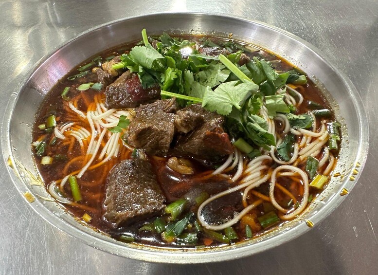 A bowl of beef noodle soup with vegetables and cilantro. 4