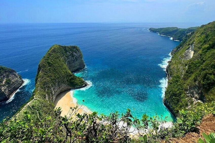 A coastal landscape with a beach, clear blue waters, and lush green cliffs. 4