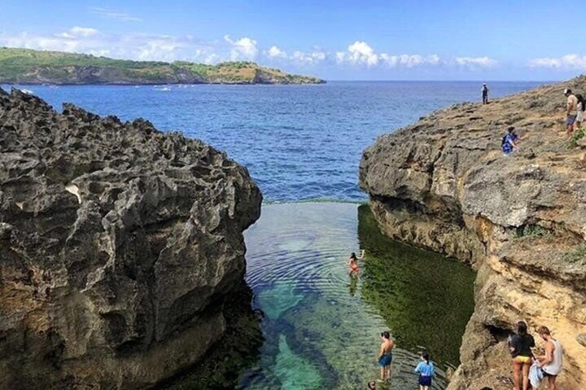 A rocky coastline with clear water and people swimming and standing on the rocks. 5