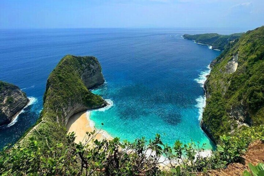 A coastal landscape with a beach, clear blue waters, and lush green cliffs. 4